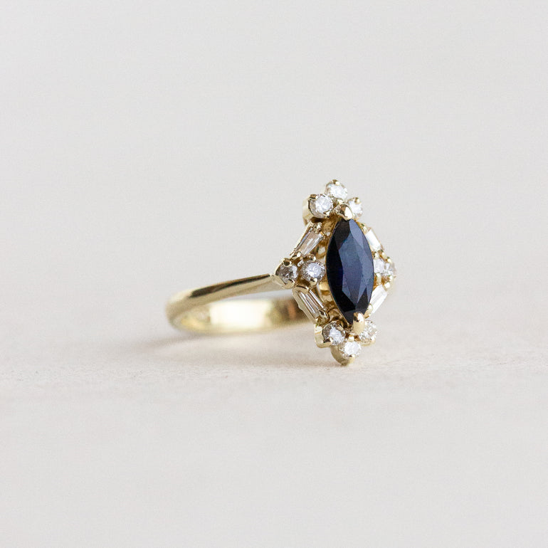 Gold ring with a blue gemstone and diamond accents on a light gray background
