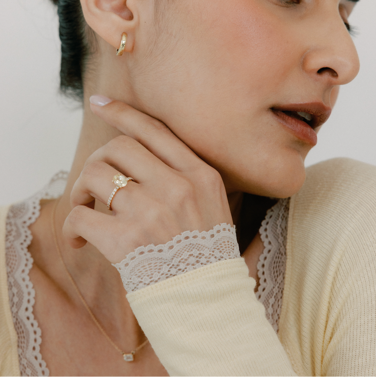 Woman wearing a gold ring and earring, with a neutral background
