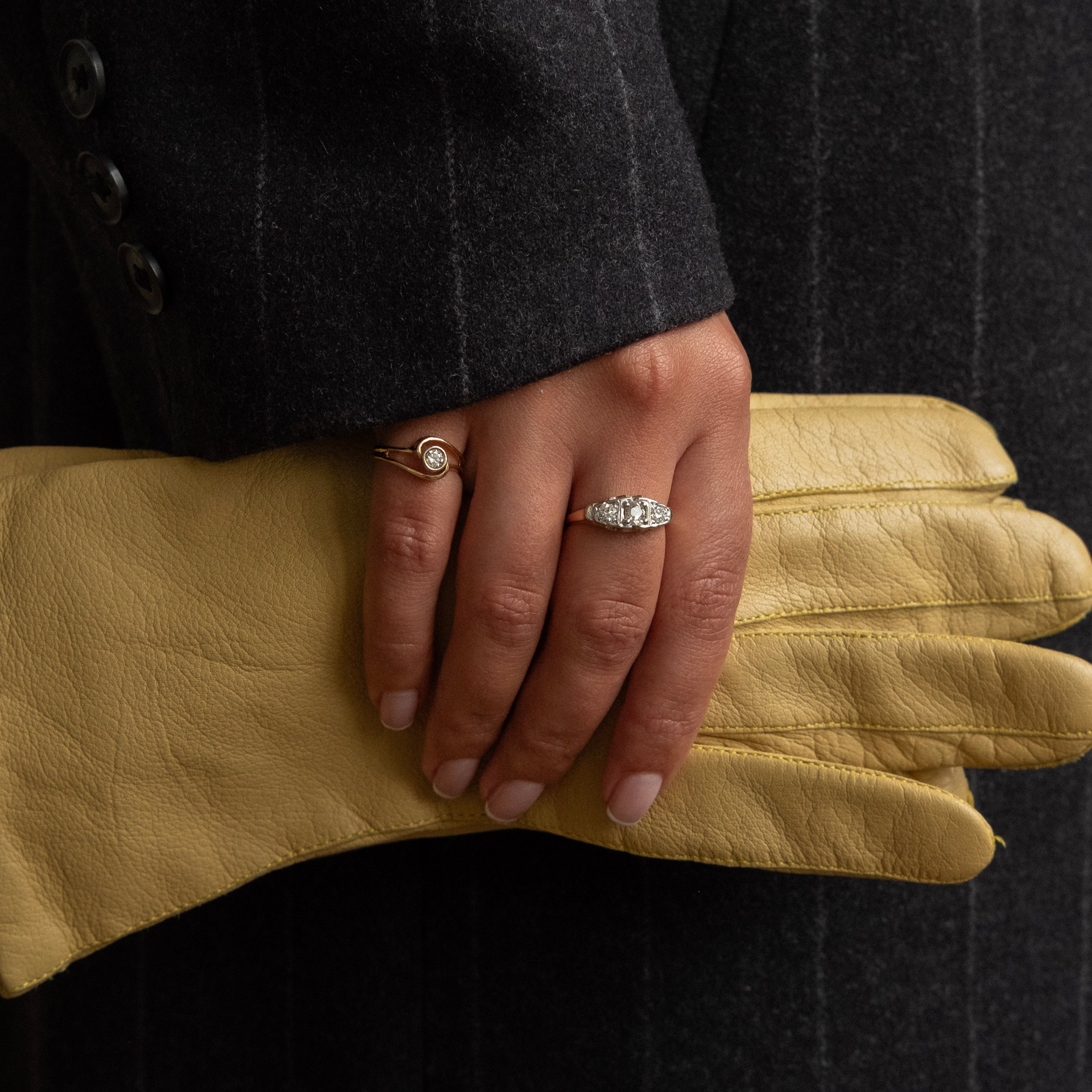 Hand wearing a yellow glove with rings, against a dark background