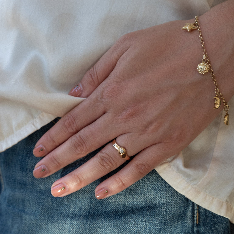 Hand wearing a gold ring and bracelet with a white shirt and blue jeans in the background