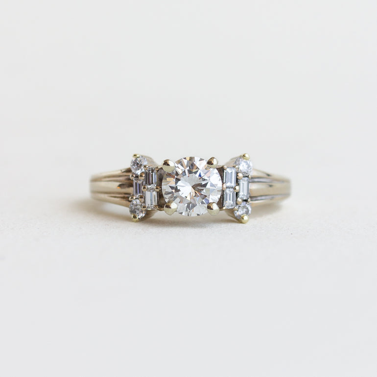 Diamond ring with a central round stone and baguette stones on a light gray background