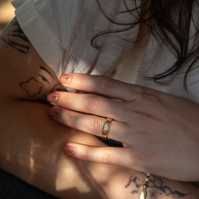 Close-up of a person's hands with tattoos and jewelry, wearing a white shirt.