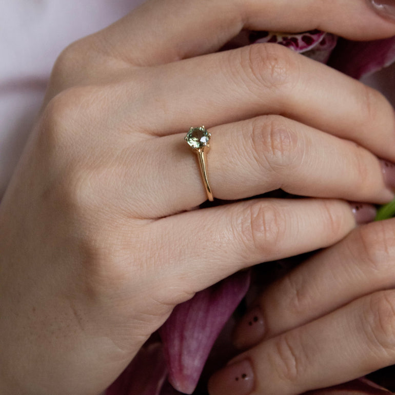 Close-up of a hand wearing a gold ring with a green gemstone, holding pink flowers.