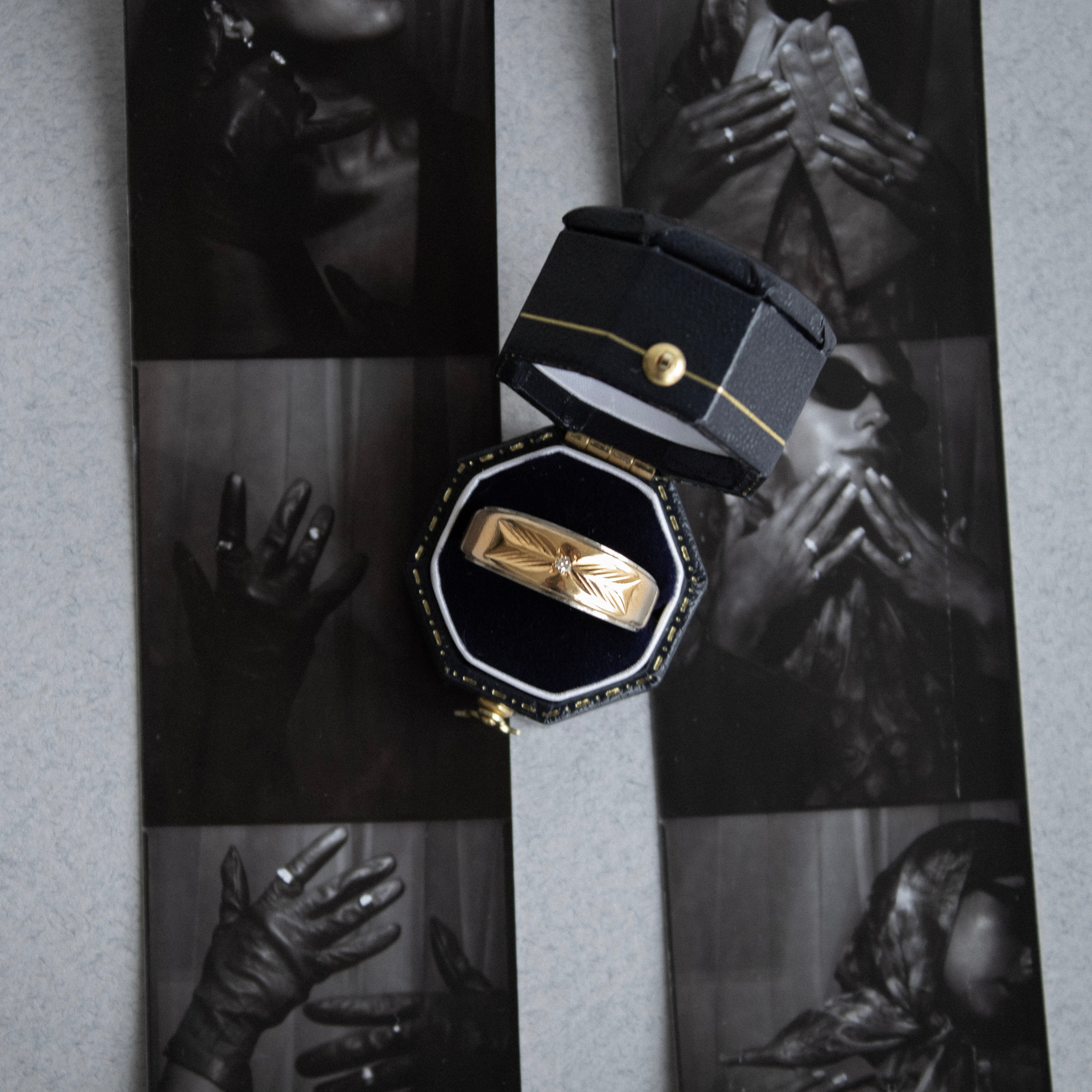 Gold ring in a black box with a collage of black and white images in the background