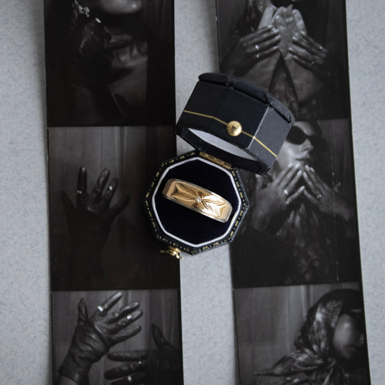 Gold ring in a black box with a collage of black and white images in the background
