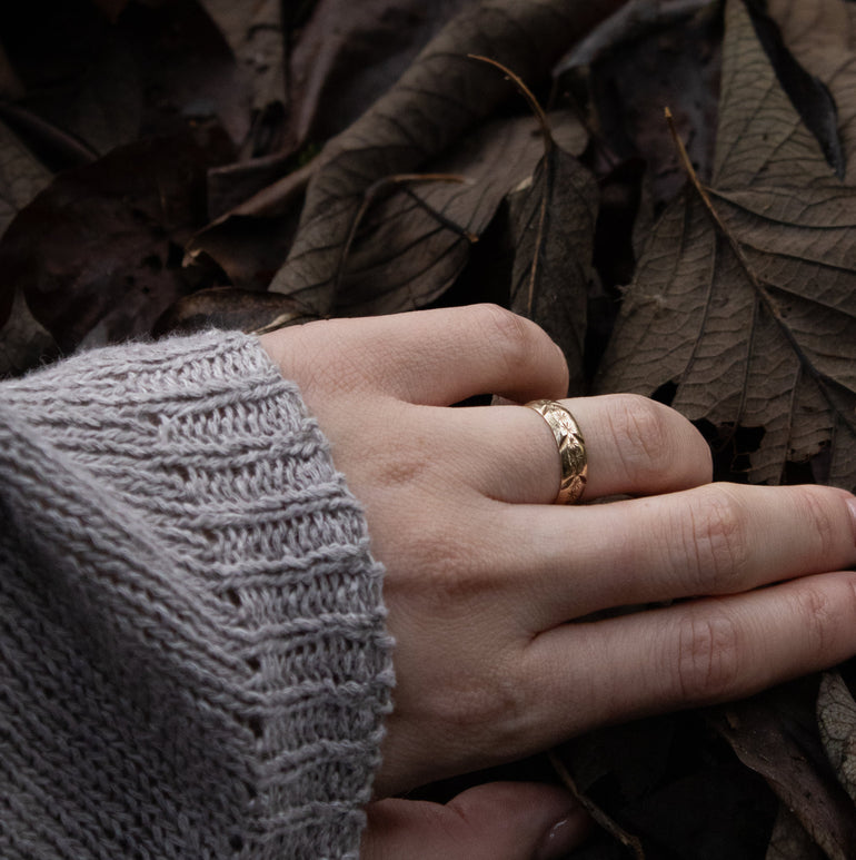 Hand with a gold ring on a background of dark leaves