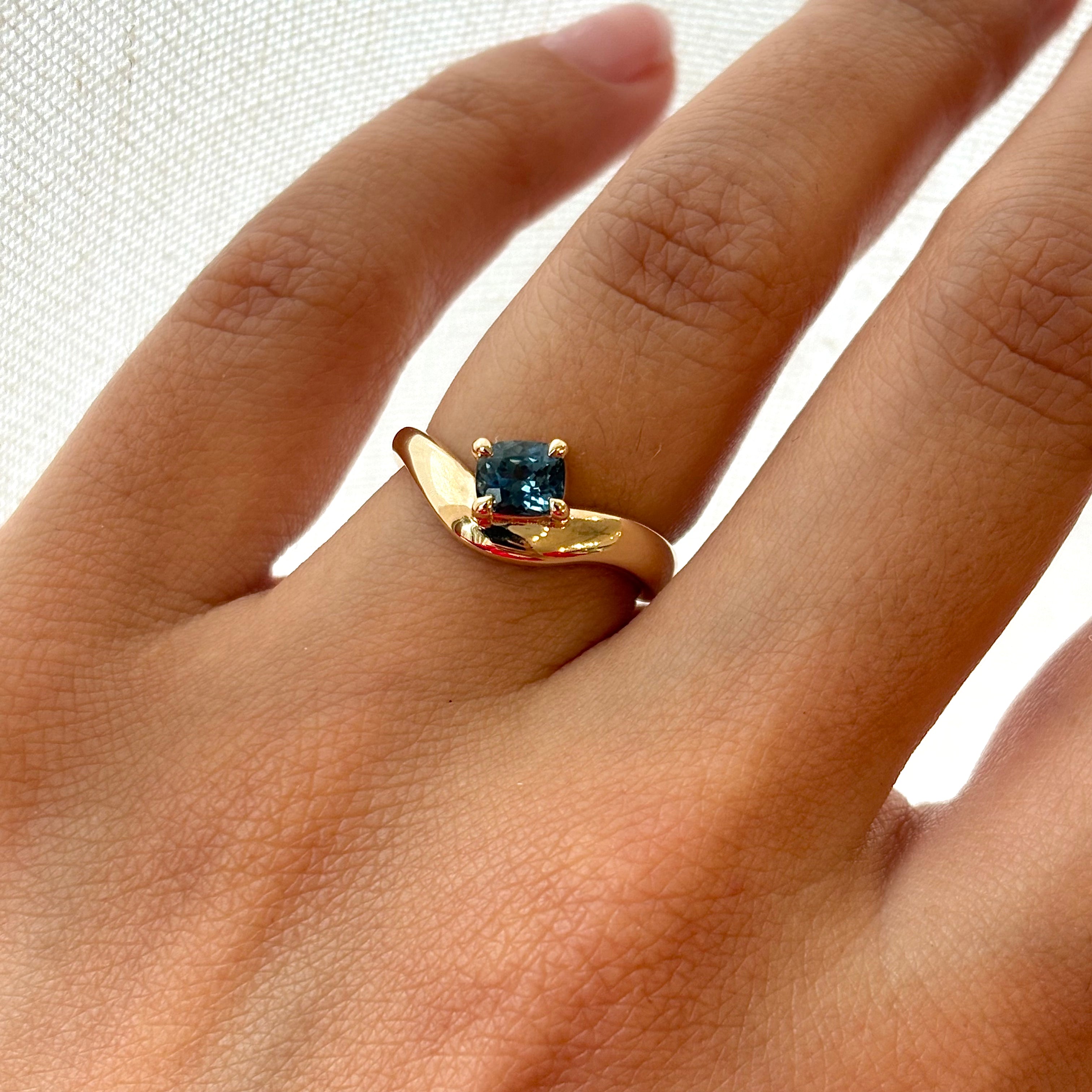 Gold ring with a blue gemstone on a hand against a white background