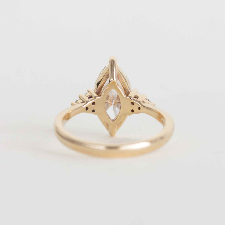 A gold ring with a marquise-cut clear gemstone in a decorative setting, photographed on a clean light gray background.