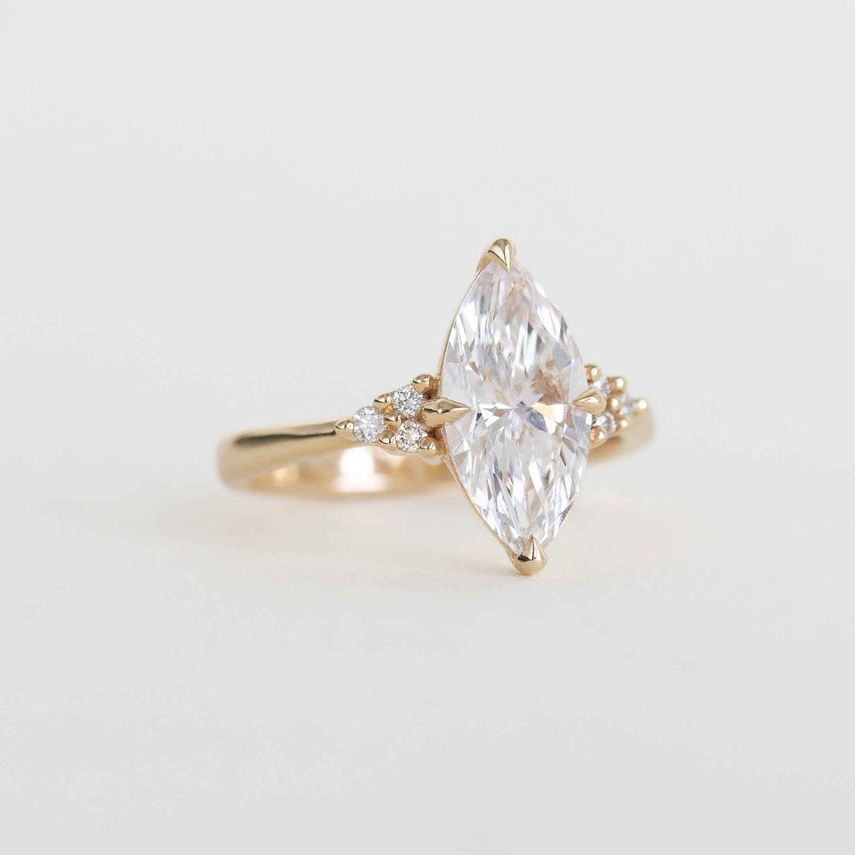 A yellow gold ring featuring a large marquise-cut clear gemstone in a prong setting, with small accent stones on either side of the band, photographed on a clean white background.