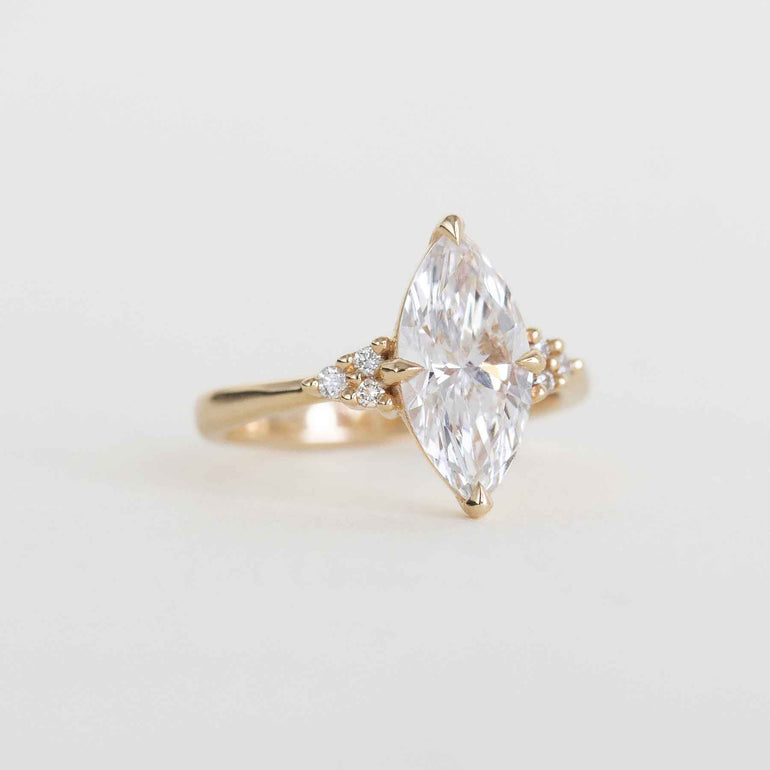 A yellow gold ring featuring a large marquise-cut clear gemstone in a prong setting, with small accent stones on either side of the band, photographed on a clean white background.