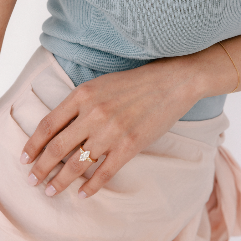 Close-up of a hand wearing a diamond ring with a light blue top and beige pants.