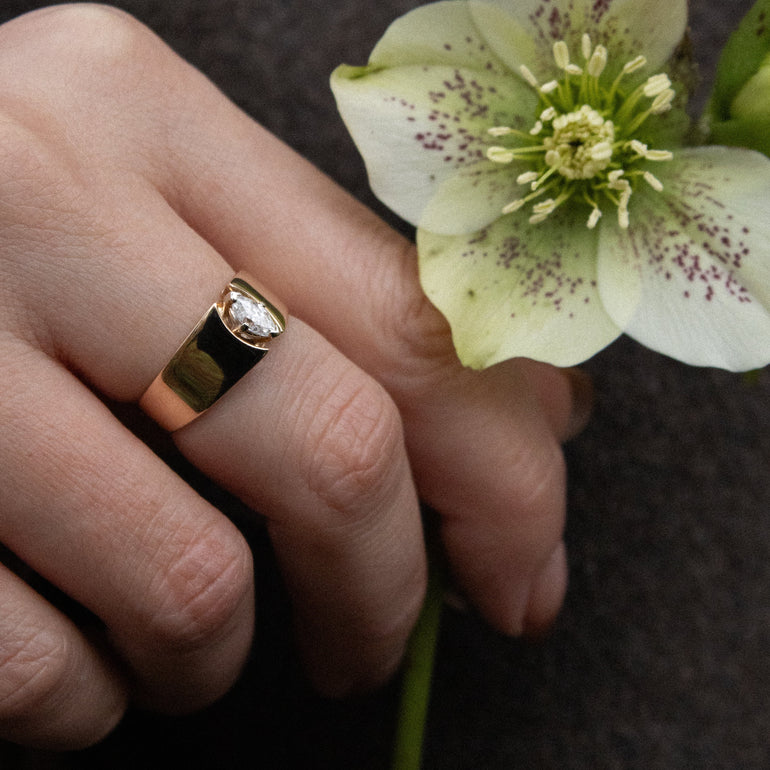 Hand holding a green flower with a gold ring on a dark background