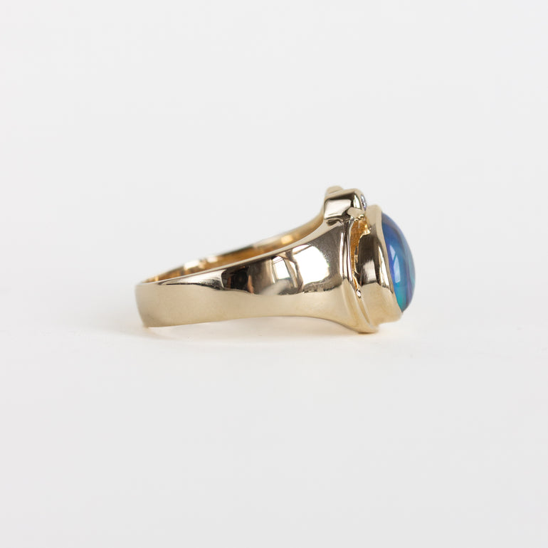 A gold signet-style ring with a polished oval blue gemstone, shown in profile against a clean white background.