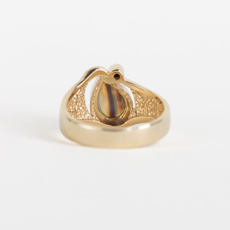 A gold ring with a textured pavé band and a central teardrop-shaped iridescent stone, photographed on a clean white background.