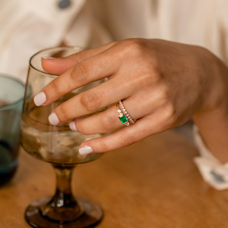 diamond eternity wedding band on hand with emerald engagement ring